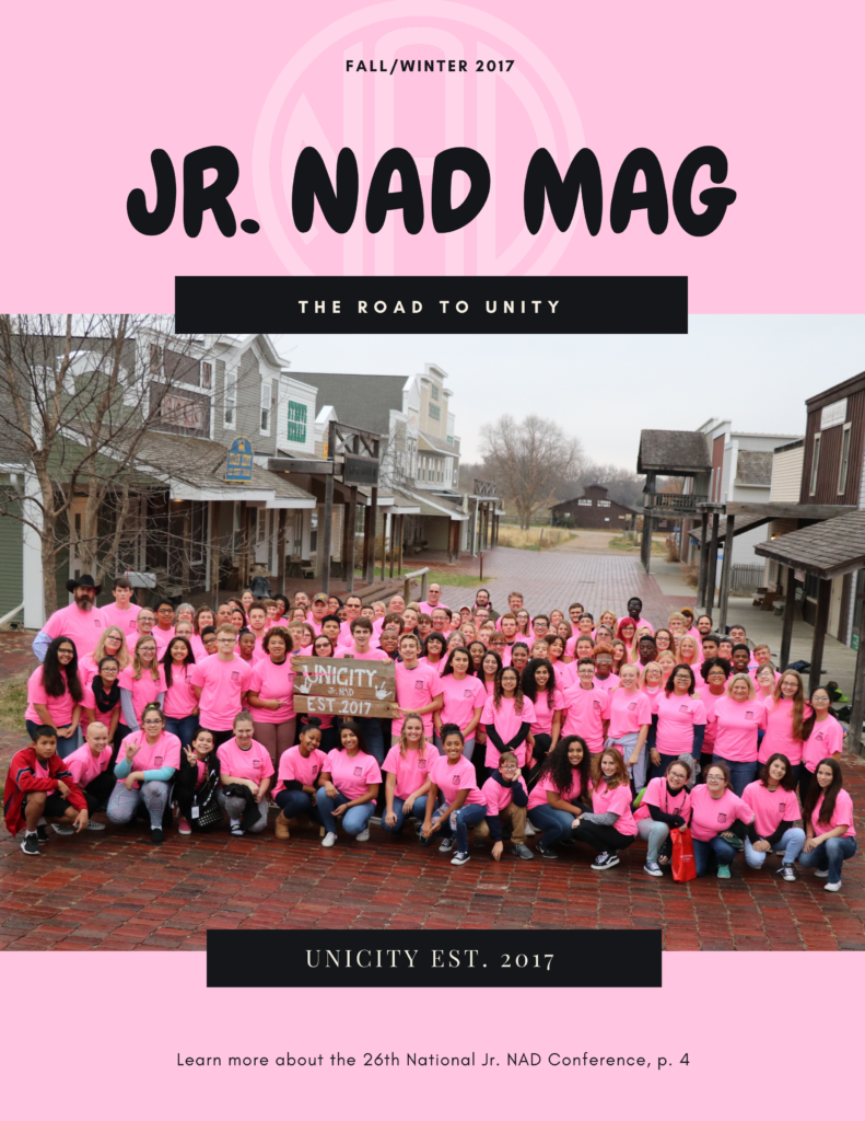 Pink background with transparent NAD logo. Text on top: "Fall/ Winter 2017, Jr.NAD MAG". There is a group photo of the Jr. NAD members with their Jr. NAD conference shirts. Black banners are taped on top and bottom. Top banner text: "The Road to Unity". Bottom banner text: "Unicity Est. 2017". Text on the bottom of the graphic: "Learn more about the 26th National Jr. NAD Conference, p.4"
